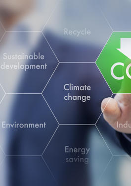 Henkilö koskettaa digitaalista käyttöliittymää, jossa korostuu CO₂-symboli sekä kasvihuonekaasupäästöihin, ilmastonmuutokseen ja kestävään kehitykseen liittyviä käsitteitä.