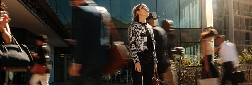 Ihminen seisoo toimistorakennuksen edessä paikoillaan, samalla kun ihmiset kävelvät hänen ohi eri puolilta