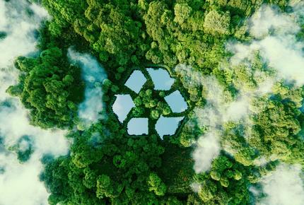 Ilmakuva vihreästä metsästä, jonka keskelle on muodostettu kierrätyssymboli vesialueiden ja kasvillisuuden avulla.
